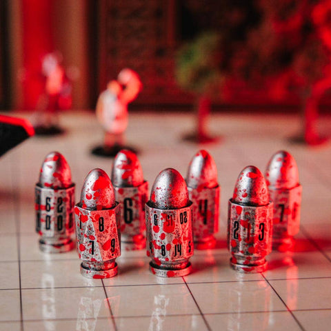 A group of metallic bullet-shaped game pieces with printed numbers, arranged on a glossy tiled surface under dramatic red lighting. A red and black textured object is partially visible on the left, with a blurred indoor background.