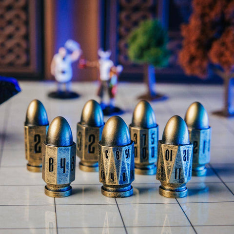 A set of metallic bullet-shaped dice with engraved numbers, arranged on a tiled surface with a blue textured pouch in the foreground and small decorative figurines in the blurred background.