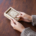 Person holding a wooden box with intricate carvings on a wooden surface