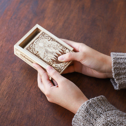 Person holding a wooden box with intricate carvings on a wooden surface