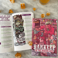 Open book with illustrations, a small book titled 'Barkeep on the Borderlands', and dice on a marble surface.