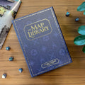 Blue book titled 'The Map Library' on a wooden surface with dice and a map.