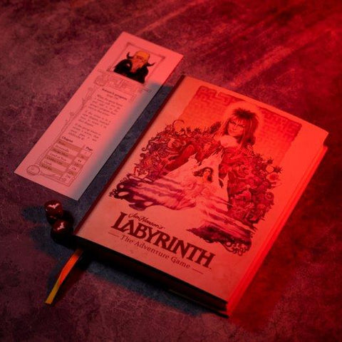 A book-style product titled "Labyrinth" for an adventure game, shown open on a textured surface under dramatic red lighting, with a printed insert card and a small die beside it.