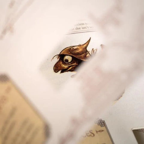 An open vintage-style book or journal with aged cream pages, featuring a small illustrated owl eye near the center and blurred text and sketches around it.
