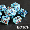 Set of blue polyhedral dice with orange numbers on a dark surface, featuring the brand 'BOTCH'.