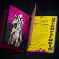 Open book with a purple cover featuring a black and white illustration of a figure with horns on a dark background.
