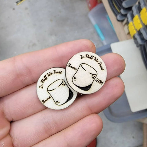 Two wooden coasters with engraved designs held in a hand, with a blurred background.