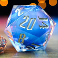 Two polyhedral dice, one blue and one clear with orange and silver numbers, on a reflective surface with blurred lights in the background.