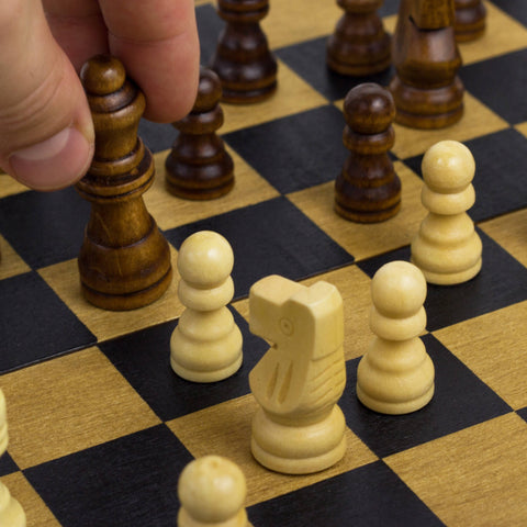 Hand moving a chess piece on a wooden chessboard