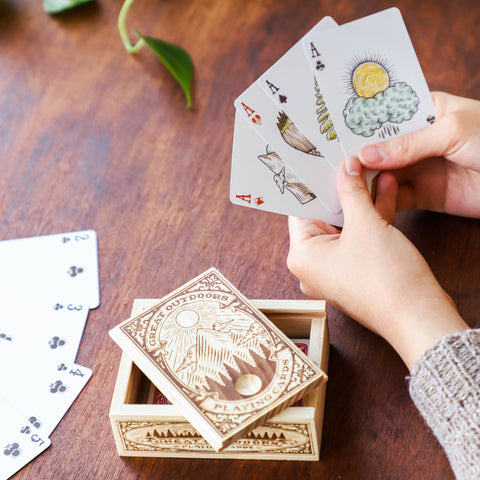 Person holding playing cards with a wooden box on a wooden table